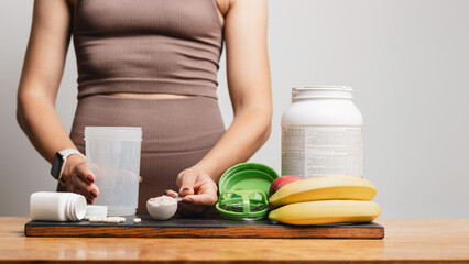 Athletic woman in sportswear holding measuring spoon with portion of whey protein powder and shaker...
