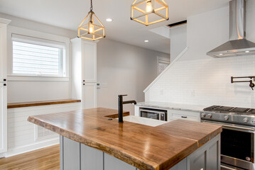 Luxury Modern White Kitchen with Organic Raw Edge Wood Countertop and Black Sleek Faucet. Subway Tile Backsplash and Pot Filler