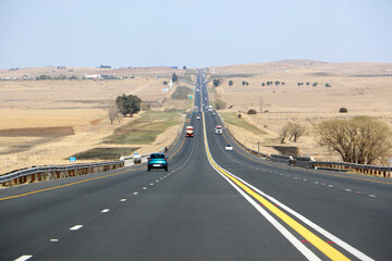 Fototapeta premium The N3 freeway from Johannesburg to Durban in South Africa, straight road to the horizon over dry landscape with cars and trucks from drivers point of view
