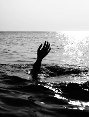 hand of person about to drown in the middle of the ocean in very dramatic black and white