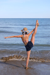 athletic girl with straw hat throws her leg in the air on the seashore