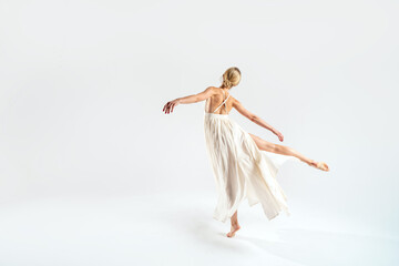 Ballet dancer dancing over studio background in maxi dress. Back view.