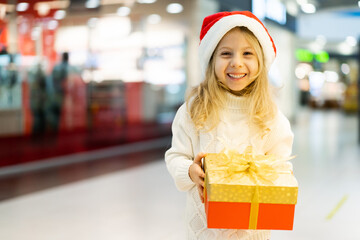 Fototapeta na wymiar a little girl in a Christmas hat with a New Year's gift in her hands at a showcase with toys. children choose gifts for Christmas. Black Friday discounts