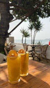 two glasses of freshly squeezed orange juice on a table in front of the sea in the morning