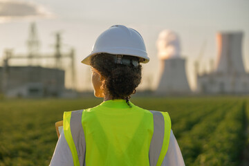 Back view of female engineer constructor stands on field on industrial enterprise background