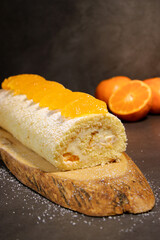 Delicious tangerine cake roll with vanilla buttercream filling on wooden plate, holiday winter dessert
