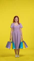 Redhaired girl holding colorful shopping bags. Full length woman in the studio on a yellow background. Vertical shot. Sale, Black Friday, advertising, discounts.