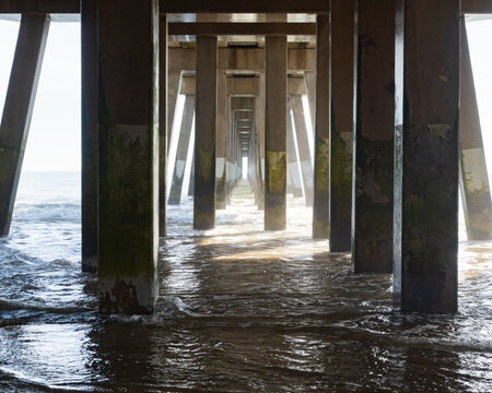 Underside of a Fishing Bridge with of a Series of Support Posts and Beams and the Water Swirling Below