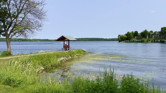 Beautiful scene of a Minnesota lake with a relaxing bench along the shore of the blue water and a motor boat in the distance, on a sunny summer day.