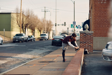 Young man tying his shoelaces before running on the sidewalk in the city