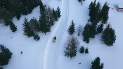 Fotobehang Top view of snowmobile driving along forest road. Clip. Snowmobile rides on beautiful snow-covered country road. Winter snowmobile trail in forest area © Media Whale Stock