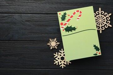 Blank Christmas invitation card and decorative snowflakes on black wooden table, flat lay. Space for text