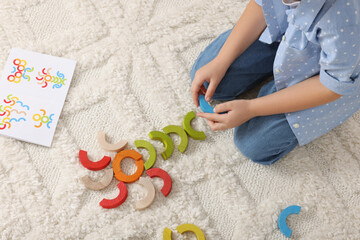 Fototapeta na wymiar Motor skills development. Girl playing with colorful wooden arcs on carpet, above view