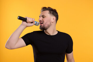 Handsome man with microphone singing on yellow background