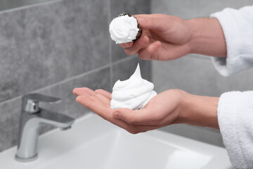 Man applying shaving foam onto brush in bathroom, closeup