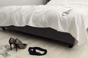 Prostitution concept. High heeled shoes, dollar banknotes and black panties on floor near bed