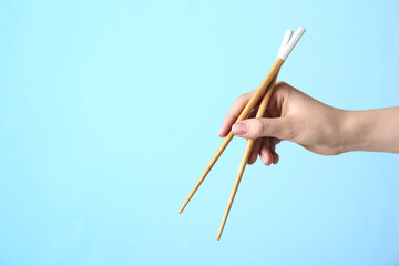 Woman holding pair of wooden chopsticks on light blue background, closeup. Space for text