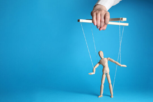 Woman pulling strings of puppet on light blue background, closeup. Space for text