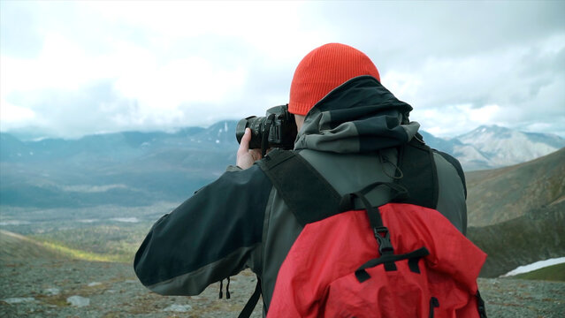 Traveler takes pictures with camera of mountain landscape with clouds. Clip. Rear view of man with backpack photographing mountain landscape. Autumn mountain landscape with traveler and camera