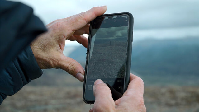 Close-up of man photographing mountain landscape with man. Clip. Phone screen is in hands of man photographing mountain landscape. Man takes pictures on phone of man in mountains
