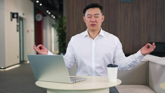 Mature Asian Man Relaxing At Office Desk With Meditation Practice And Mudra Gesture. Business Person In White Collar Shirt Regaining Energy And Harmony During Working Day On Wireless Laptop.