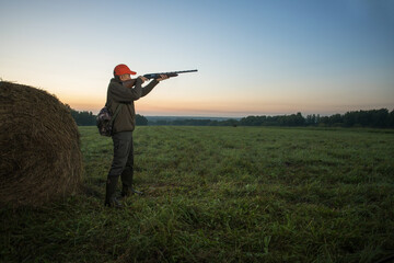 A hunter in camouflage and a shotgun in his hands in the early morning. Hunter aiming with rifle