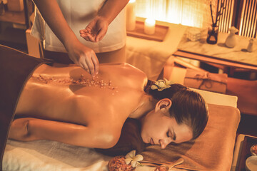 Woman customer having exfoliation treatment in luxury spa salon with warmth candle light ambient. Salt scrub beauty treatment in Health spa body scrub. Quiescent - obrazy, fototapety, plakaty