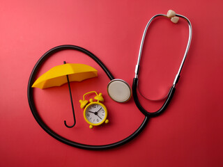 Top view stethoscope,alarm clock and yellow umbrella on a red background