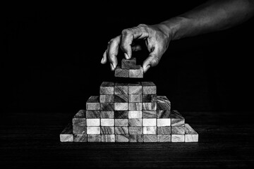Hand placing wooden block tower stack in pyramid stair step with caution to prevent collapse or...