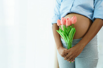 Portrait of happy beautiful American - African ethnicity pregnant woman holding a tulip bouquet standing near window close up. Mental health care and wellbeing in pregnancy woman.
