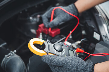 Obraz premium Close-up hand auto mechanic using meter to check car battery fail problem to change repairing and fix car and maintenance servicing.