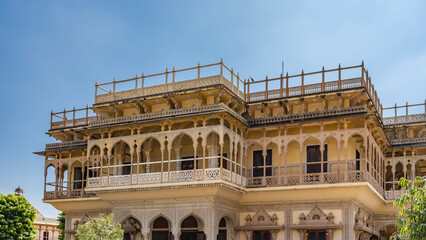 Obraz premium Details of ancient Indian architecture. The upper floors of the City Palace against a clear blue sky. Galleries with elegant columns, arches, carved railings. Fence along the edge of the roof. Jaipur.