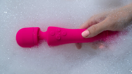 Woman lies in a bubble bath and uses a vibrator.  - obrazy, fototapety, plakaty