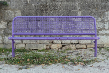 purple park bench made with metal frame against stone wall in the park