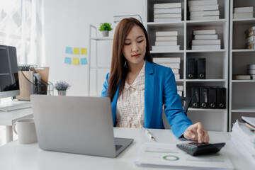 Young Asian business woman in finance presses calculator, business woman works in finance, financial planning for startup company and checking financial statements. Financial management concepts.