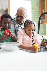 Happy african american grandfather and grandchildren washing vegetables in kitchen, slow motion