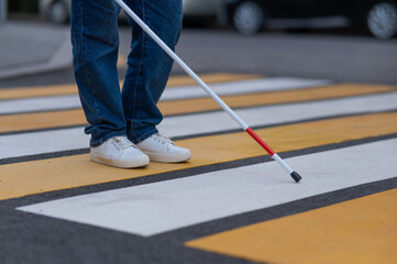 Close-up of the legs of a blind woman crossing the road at a crosswalk with a cane. 