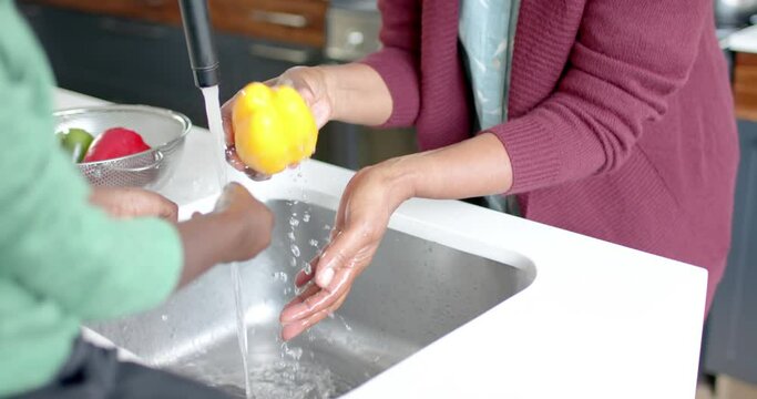 Happy african american grandmother and grandson washing vegetables in kitchen, slow motion