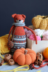 Knitted toy fox, yarn balls and autumn decorations on a gray background with space for text. Cute amigurumi toy. 