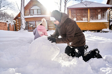 A family builds a snowman out of snow in the yard in winter.