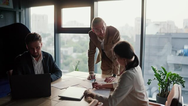 Young Boss in a modern office, a blond man in glasses with a light brown beard tells his colleagues what they need to do and thinks about upcoming issues. Modern office with panoramic windows