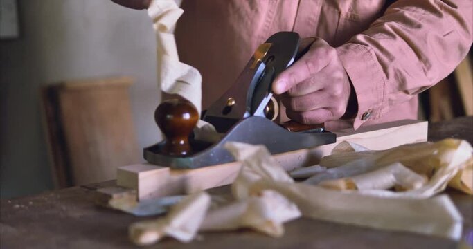 Master carpenter works with a hand plane on wood with thin shavings