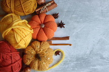 Autumn still life with woolen yarn balls, crocheted pumpkins, cinnamon sticks and anise on grey background with copy space. Cozy autumn concept. 