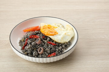 Nasi Goreng Cumi Hitam or Black Squid Fried Rice, served in white plate on wooden table

