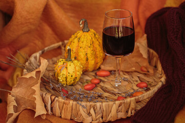 Glass of red wine on wooden table decorated with pumpkins and dried leaves outdoor. Autumn...