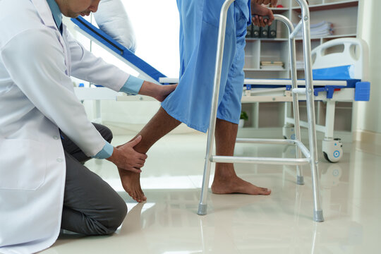 Physical therapist helps a male patient use a walker to practice walking. Support yourself from recovery from sore legs and ankles. Physical therapy service concept.