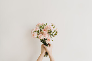 Girl's hand hold elegant pink carnation flowers bouquet on neutral white background. Aesthetic...
