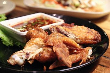 Fried chicken wings with fish sauce and Thai dried chilli dipping sauce (Nam Jim Jaew) serve on black plate and on wooden table, close up, selective focused.
