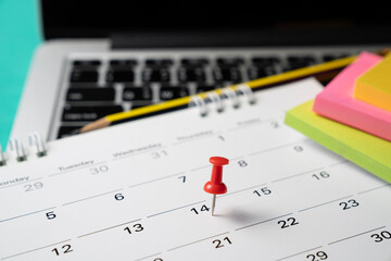 close up pin on calendar with laptop on the table background, planning for business meeting or travel planning concept