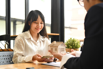 Happy female client making sale purchase, signing contract with real estate agent. First property purchase and home ownership